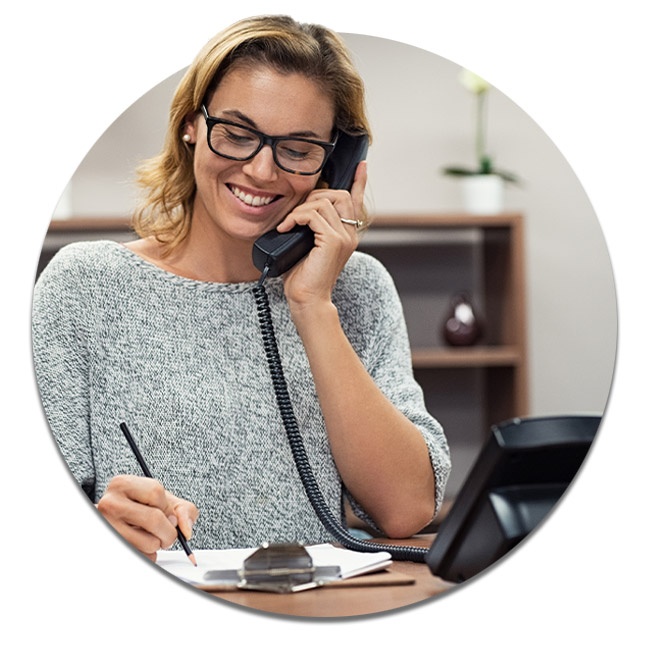 Casual smiling business woman sitting at desk making telephone call and taking note.