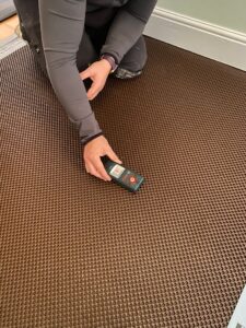 A Property Conservation Services technician using a stud detector over the floor membrane before nailing it down