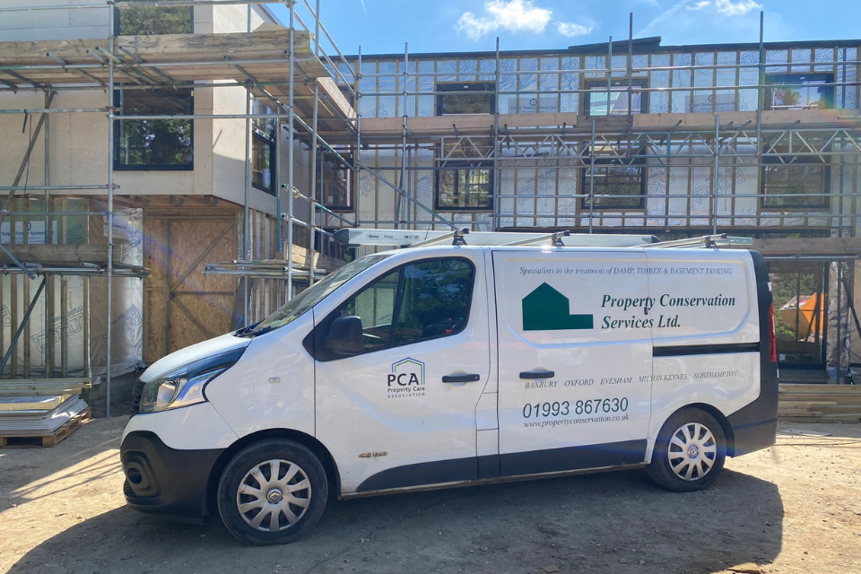 A Property Conservation Services van parked in front of a large commercial building undergoing work for common damp problems