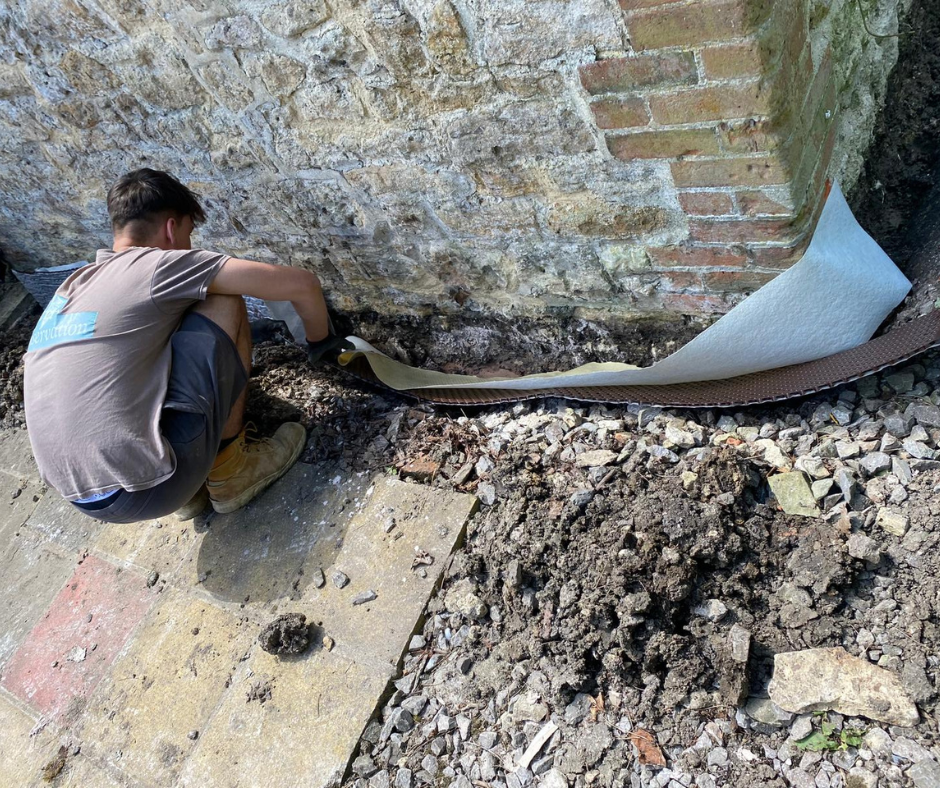 Dampproof technician's apprentice, Alan, trimming excess Geo-Drain outside