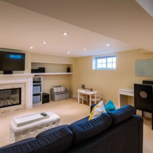 A beautifully converted basement showing a sofa, and a TV on the wall. There's also a desk and office chair in the space.