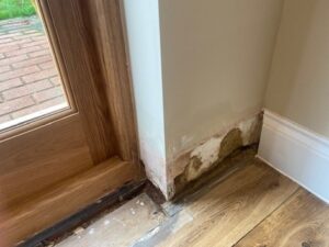 Missing skirting board from by the back door, showing damp damage in the wall