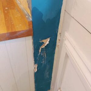 Peeling paint and blown plaster on an interior wall by a kitchen door