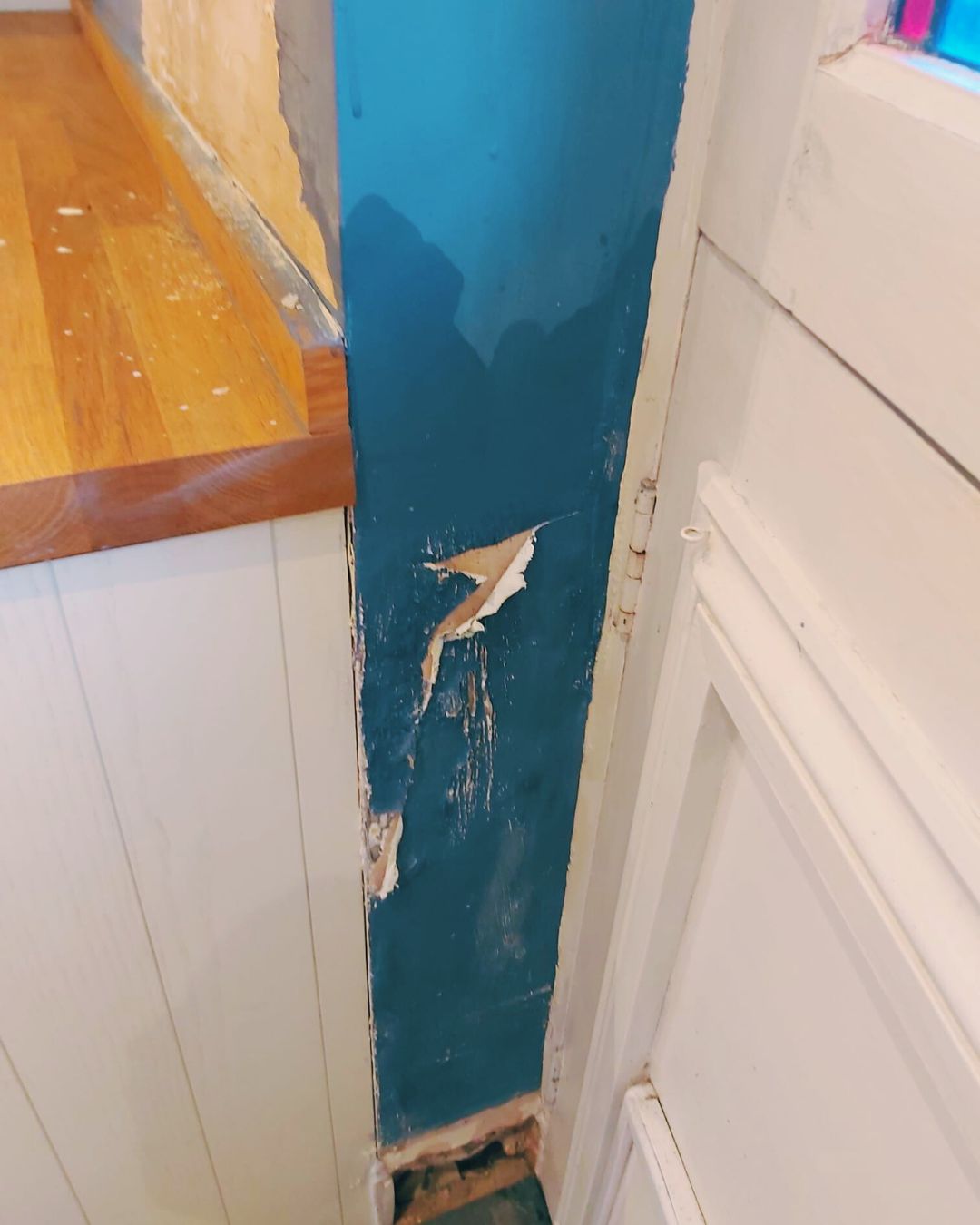 Peeling paint and blown plaster on an interior wall by a kitchen door